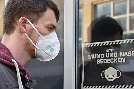 Mann mit medizinischer Maske vor Fensterscheibe